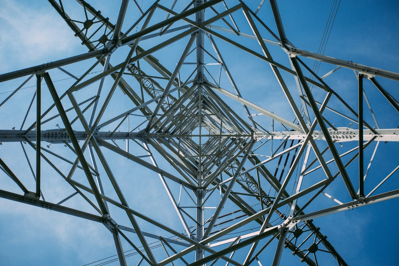 Estrutura metálica de uma torre de transmissão vista de baixo contra o céu azul. Imagem ilustrativa.