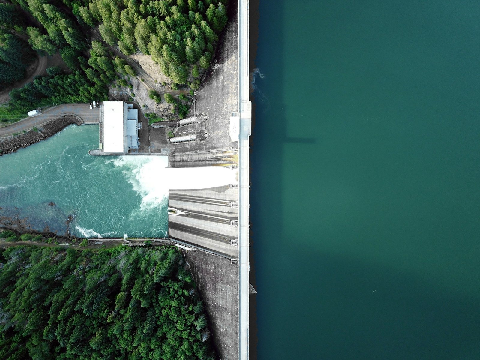 Vista aérea de uma barragem com reservatório e água liberada no rio